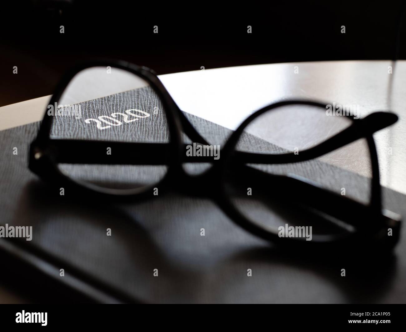 Schwarzes Tagebuch 2020 mit Lesebrille auf weißem Tisch Stockfoto