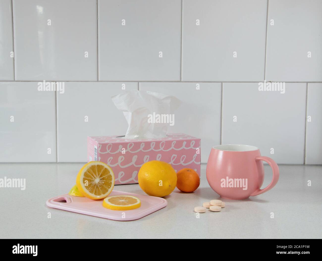 Geschnittene und ganze frische Zitrone für gesunden Tee in rosa Becher mit Taschentuchbox Stockfoto