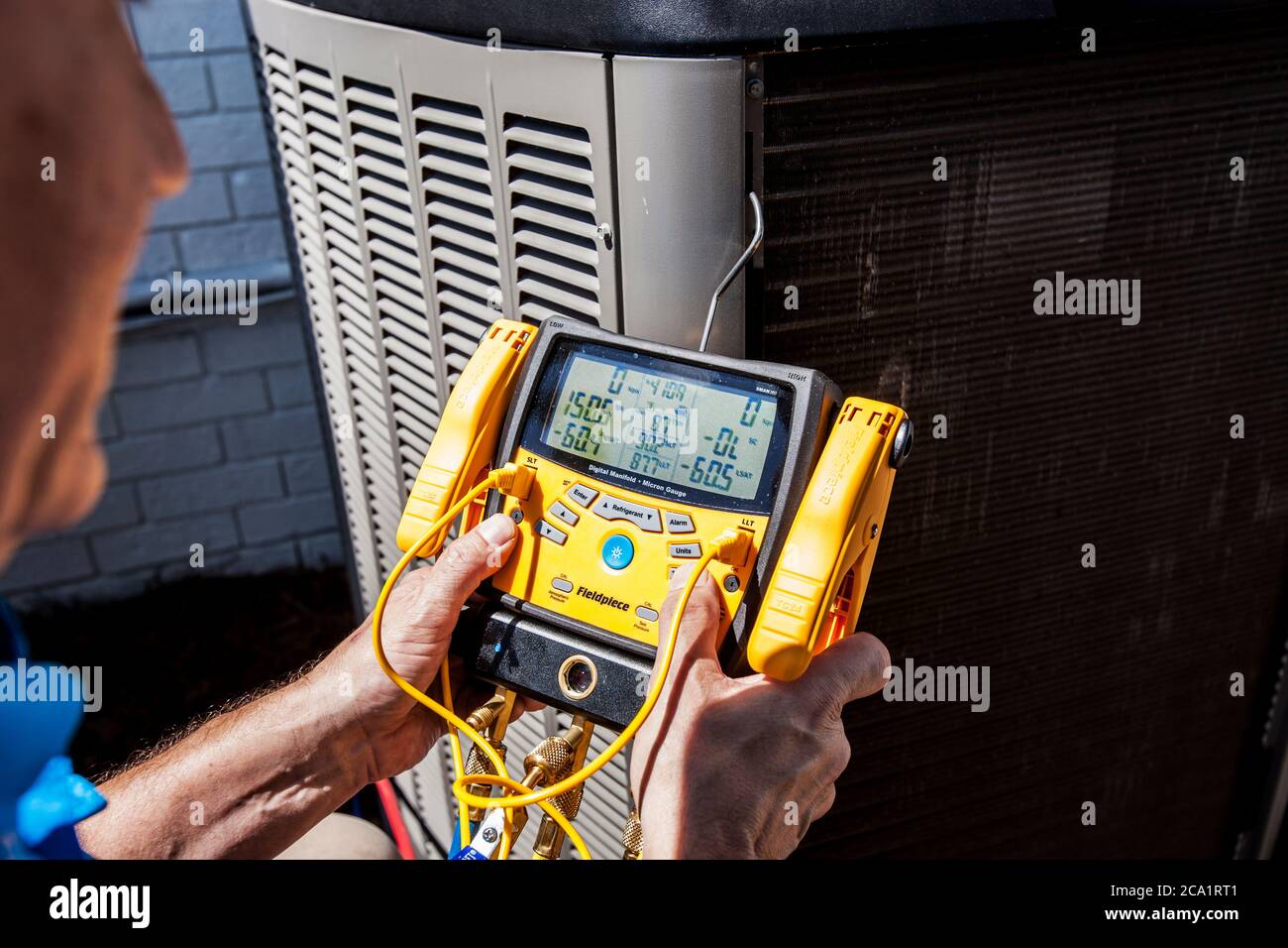 Die Werkstatt arbeitet mit einem tragbaren digitalen Feldpiece-Instrument an der Klimaanlage eines Heims im Freien Stockfoto