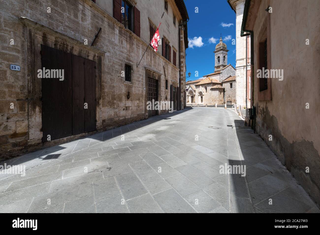 Ikonisches toskanisches Stadtbild, mit einer Stadtstraße, die zu einer alten römischen Kathedrale unter einem blauen Sommerhimmel mit spärlichen Wolken führt Stockfoto