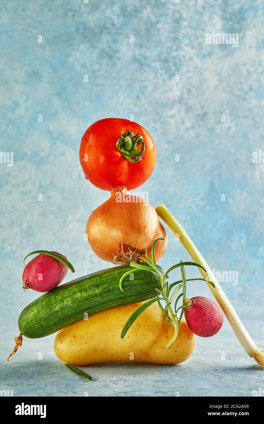 Eine Gourmet-Food-Komposition mit buntem Gemüse auf blauem Hintergrund, für eine lustige Gastronomie und vegetarisches Rezept. Gleichgewicht schwimmende Lebensmittel Balanc Stockfoto