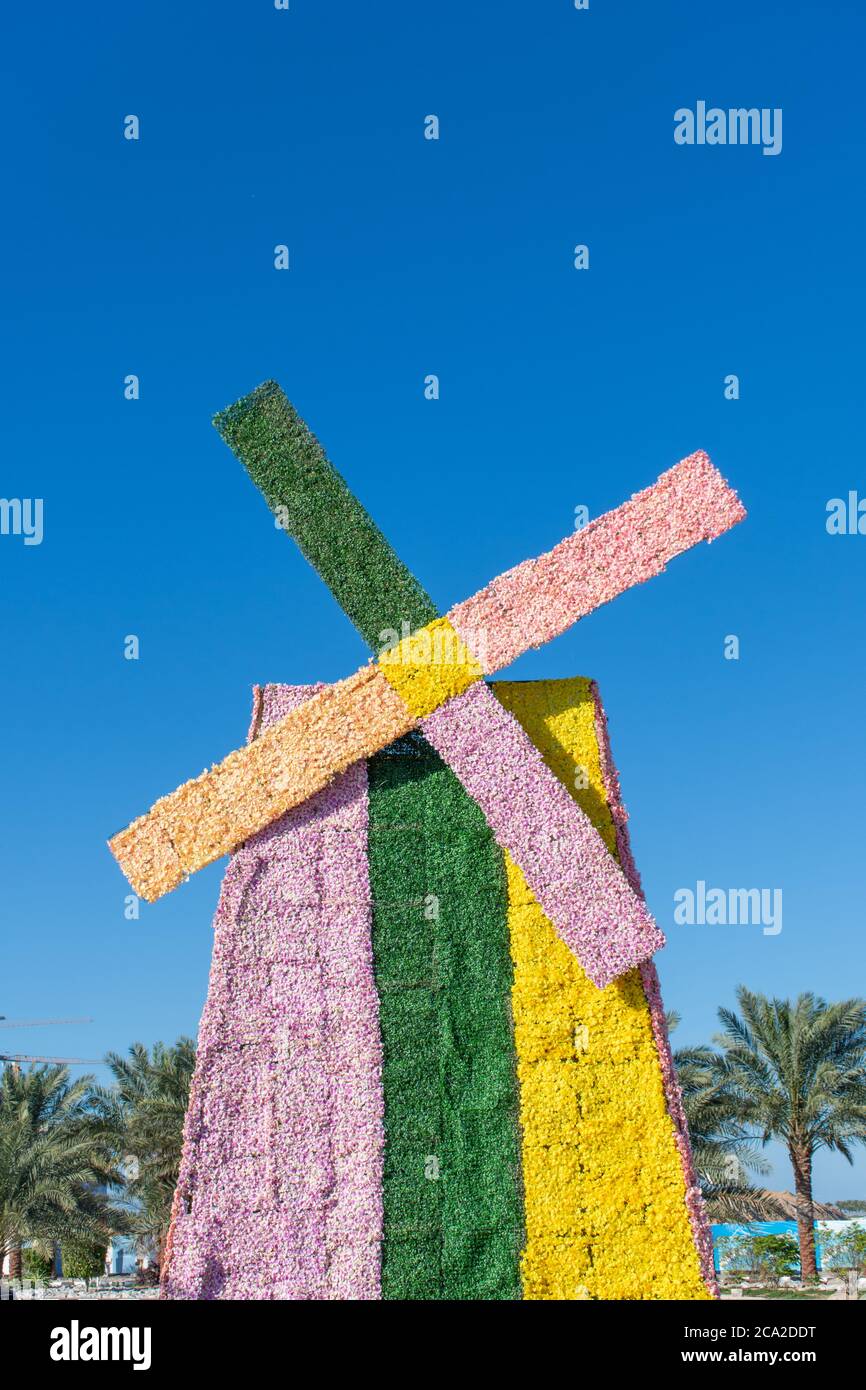Eine in Rosa, Grün und Gelb gefärbte Blumenwindmühle an einem sonnigen Tag am blauen Himmel bei einer Feier im Freien. Niederländisches oder niederländisches Thema oder Konzept. Stockfoto