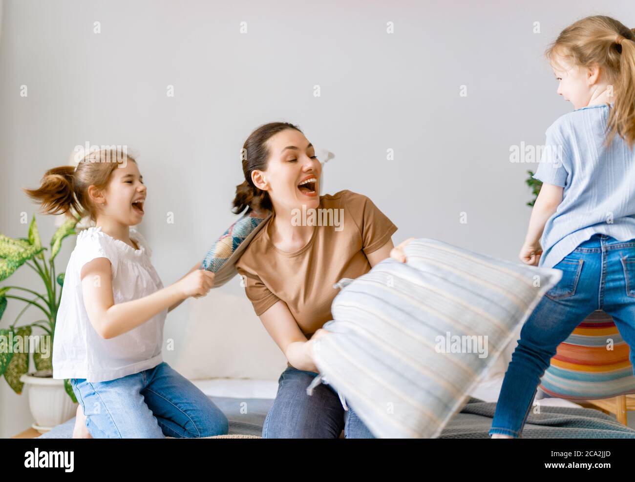 Glückliche, liebevolle Familie! Die Mutter und ihre Kinder kämpfen zu Hause auf dem Bett mit Kissen. Stockfoto