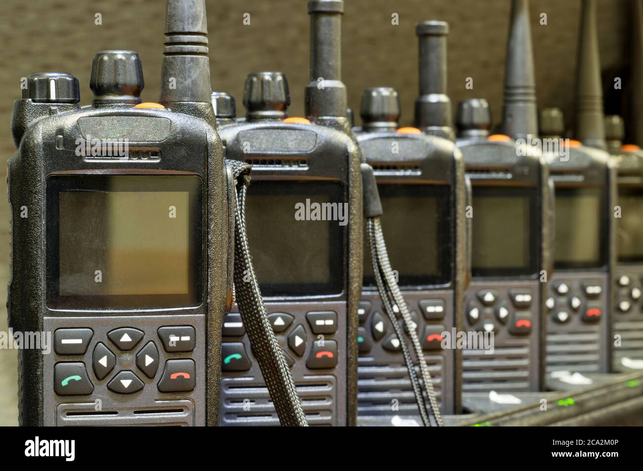 Schwarze Walkie-Talkies standen in einer Reihe, die aufrecht auf Ladestationen mit Fokus auf den Vordergrund saßen. Stockfoto