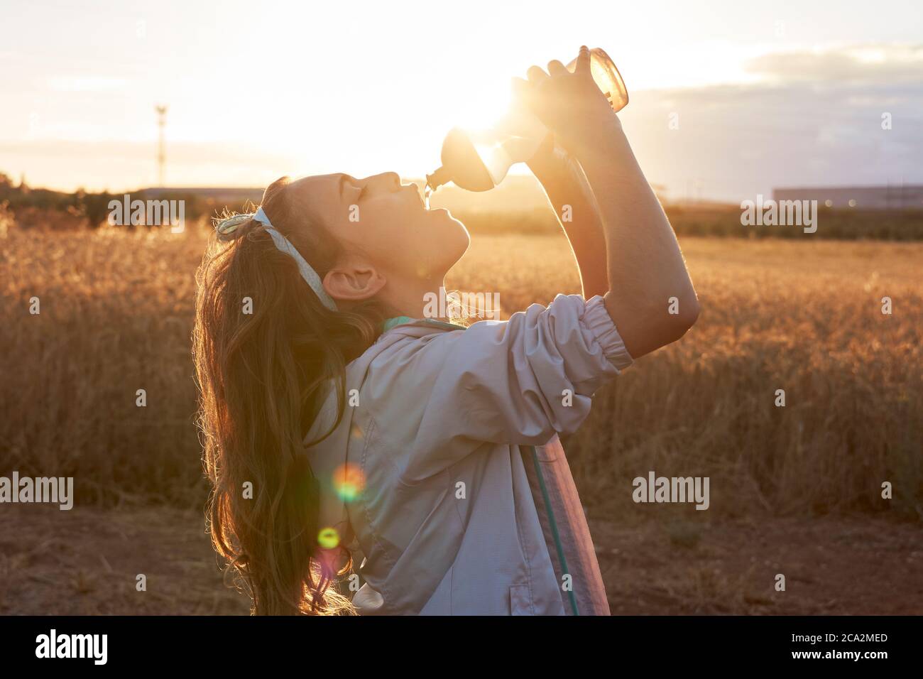 Mädchen trinkt Wasser aus einer Flasche bei Sonnenuntergang Stockfoto