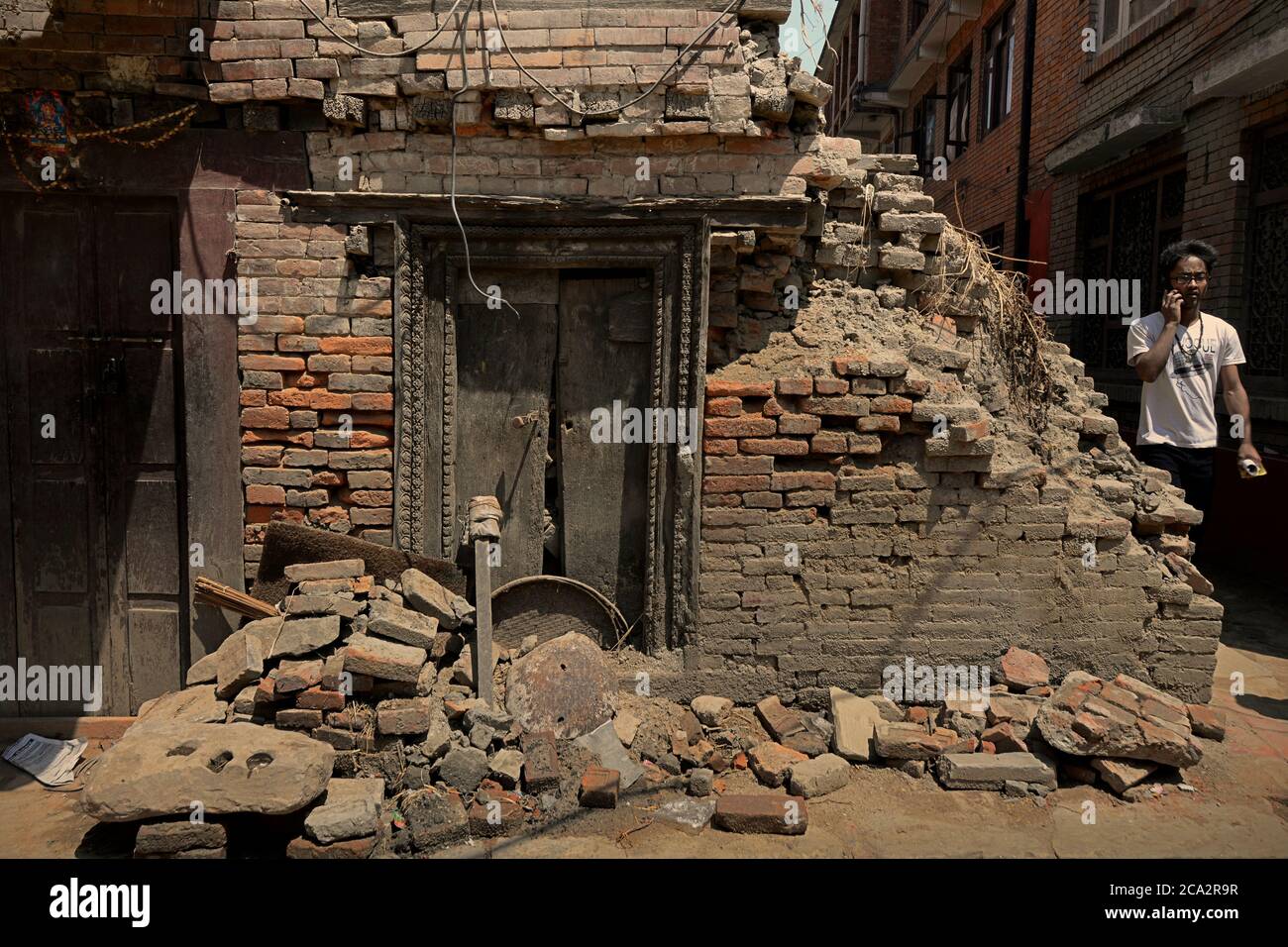 Ein Bhaktapur-Bürger, der auf einer Wohnallee spaziert, in der Gebäude durch die Erdbeben von 2015 in Nepal beschädigt wurden. Bhaktapur, Nepal. Stockfoto
