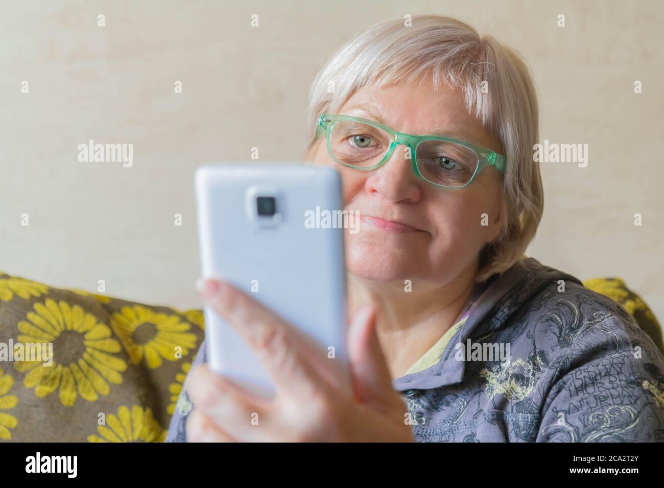 Ältere Frau, die ein Mobiltelefon für die Verbindung mit Verwandten verwendet. Ältere Frau nimmt Selfie. Lady mit Smartphone in der Hand zu Hause. Weiblich, die das Telefon benutzt Stockfoto