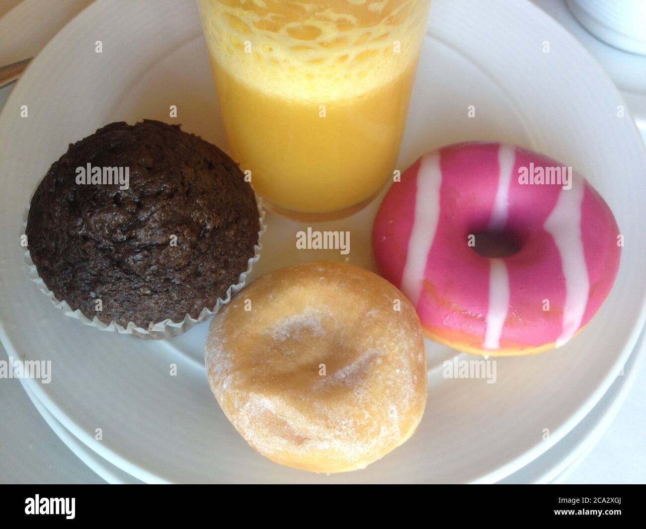 Ungesund Super-süßes Frühstück. Mehrere Kuchen um Orangensaftglas. Stockfoto