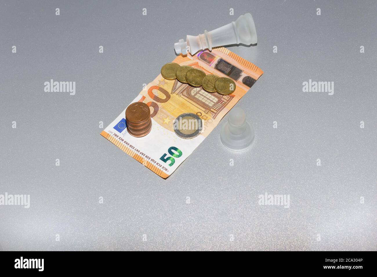 Euro-Münzen und 50 Euro Banknote, mit Schachkönig und Spielfiguren auf isoliertem grauen Hintergrund. Business bankrott, sparen und Finanzen Konzept. Stockfoto