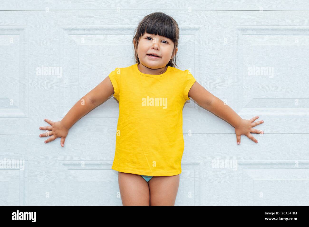 Liebenswert kleines Mädchen mit schwarzen Haaren trägt ein gelbes Hemd lehnt vor weißem Hintergrund. Stockfoto