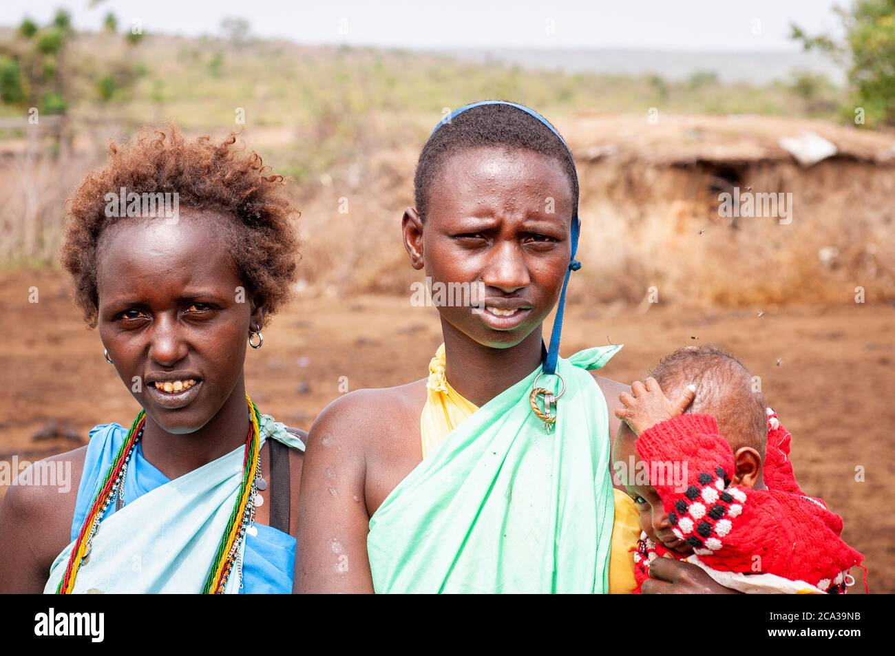 Zwei junge Maasai Frauen, mit einem Baby, in traditioneller Kleidung, in einem maasai Dorf. Maasai Mara National Reserve. Kenia. Afrika. Stockfoto