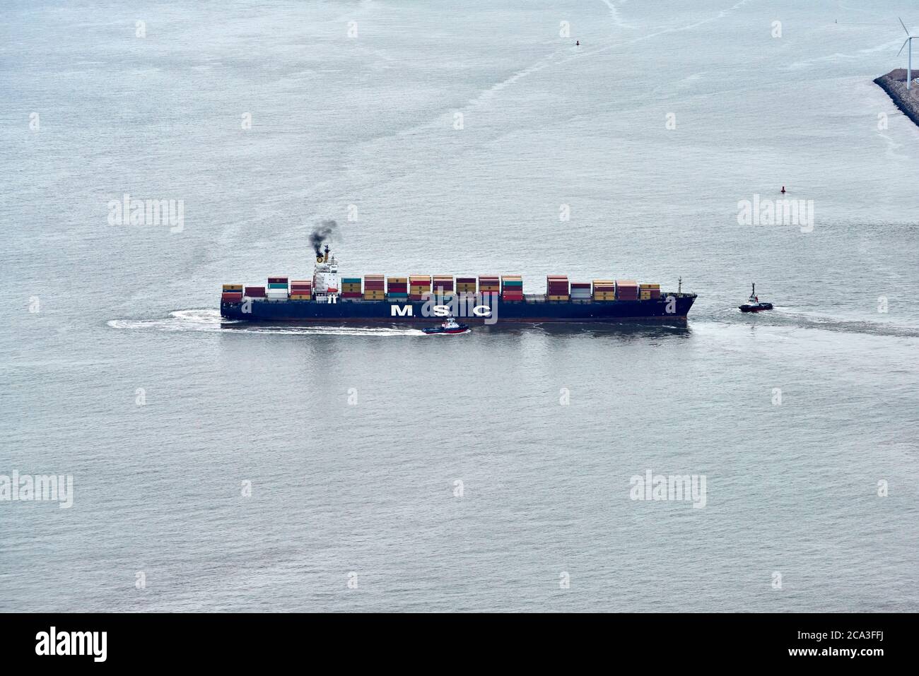 Ein Containerschiff, das von zwei Schleppern in der Mündung des Flusses Mersey, Liverpool Port, Großbritannien, manouvered wird Stockfoto