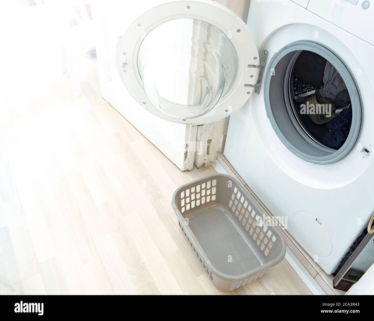 Eine Waschmaschine mit geöffneter Tür und ein kleiner Plastikkorb für die frisch gewaschene Wäsche. Das Innere eines Hauses. Hausarbeiten und Reinigung Stockfoto