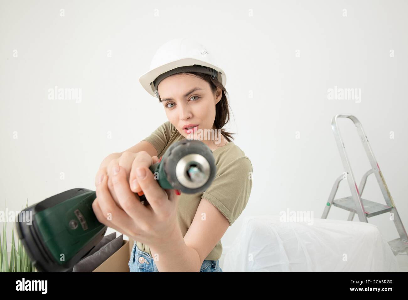 Portrait von selbstbewussten jungen Frau in Hardhat mit Power-Schraubendreher während der Renovierung in neue Wohnung Stockfoto
