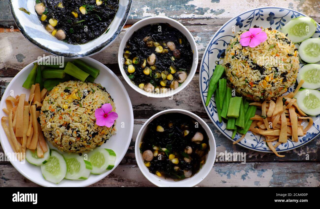 Draufsicht zwei Teller gebratener Reisgerichte mit Gemüse wie Gurke, Bambusshoot, Okra und Algensuppe zum Familienessen zum Mittagessen, leckeres veganes Essen Stockfoto