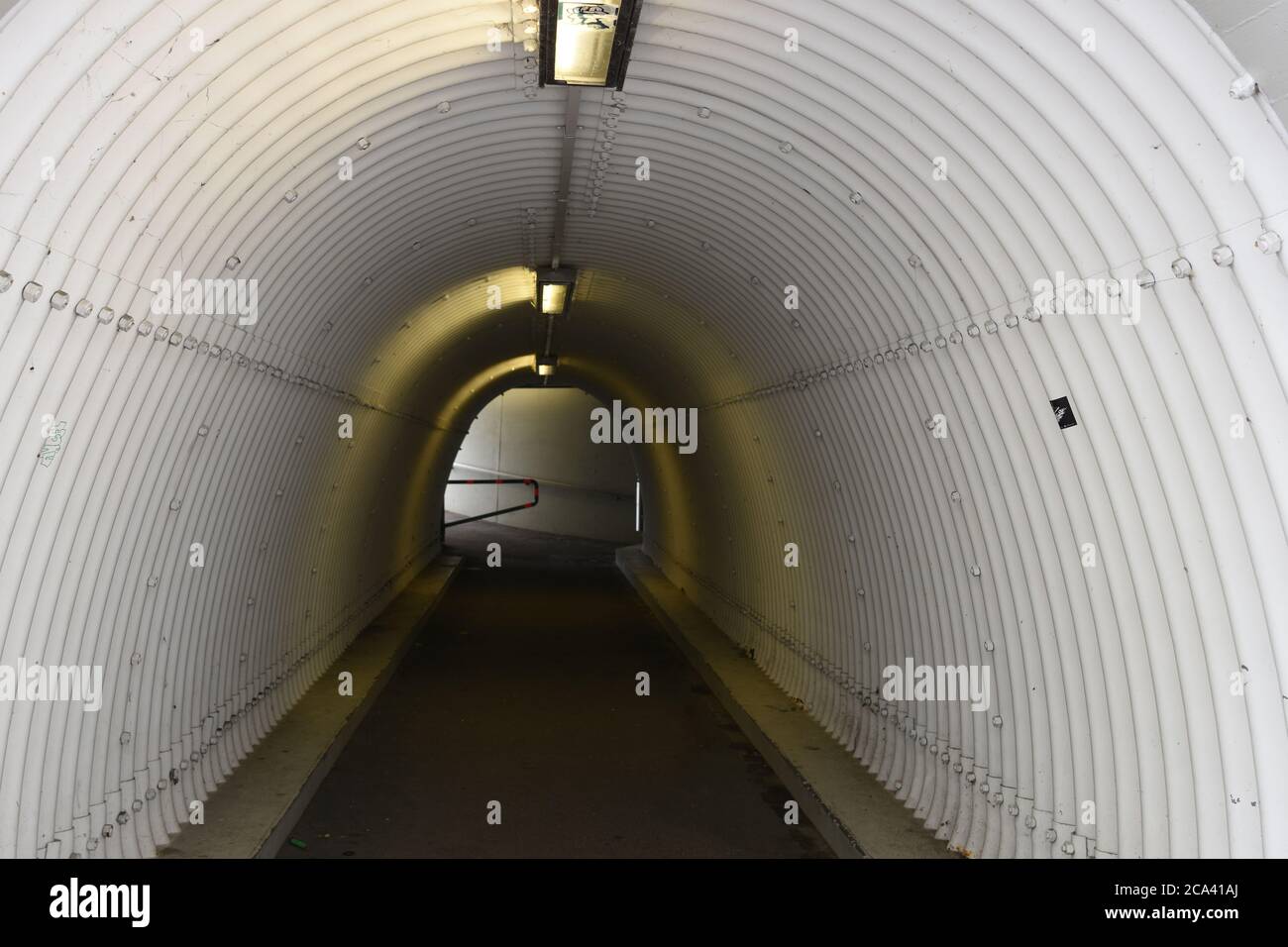 Städtische Fußgängerunterführung oder Unterführung unterhalb der Autobahn. Passage hat gewellte Oberfläche der Wände in Form von weißen Tunnel mit Deckenleuchten. Stockfoto