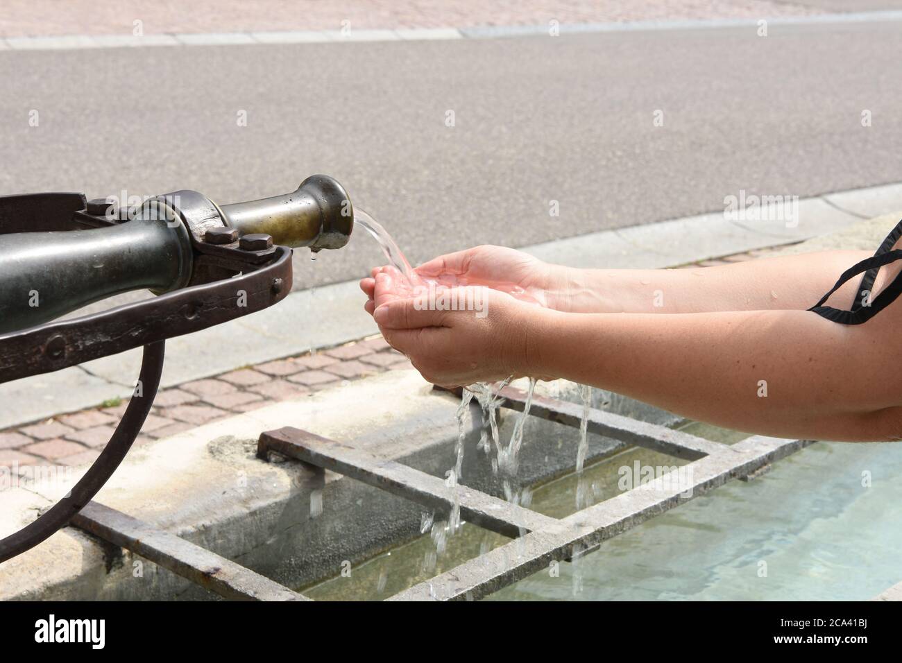 Sammeln fließendes Wasser in den Händen, um aus dem öffentlichen Brunnen zu trinken, während eine Pause bei heißem Sommerwetter auf einem Wanderweg im Dorf Uitikon. Stockfoto