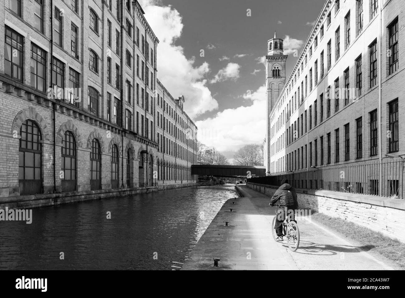 Mann auf dem Fahrrad entlang einer Straße neben Leeds und Liverpool Canal und Salts Mill, Bradford, West Yorkshire, England, Großbritannien. Stockfoto