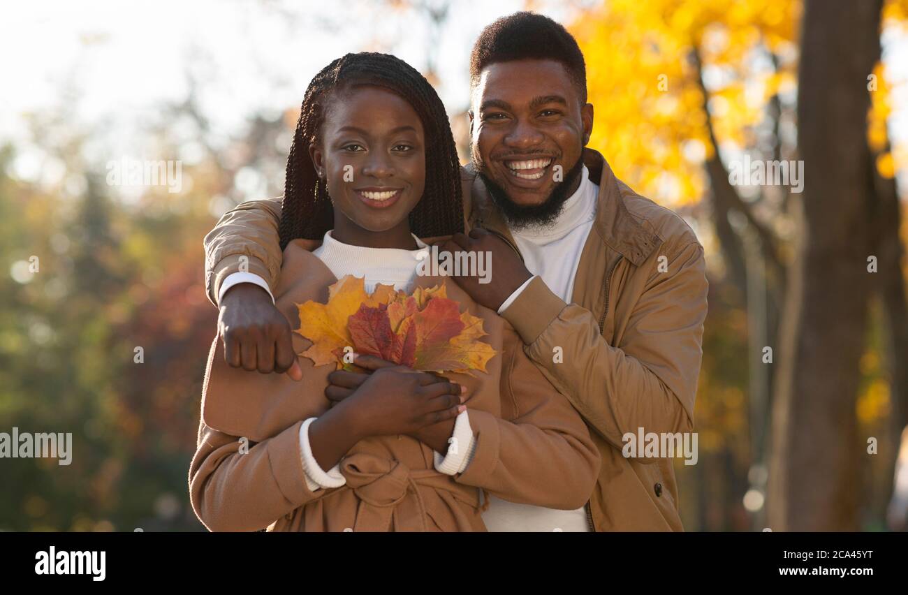 Schwarzes Millennial-Paar mit einem Laubhaufen, der sich im Herbstpark umarmt Stockfoto