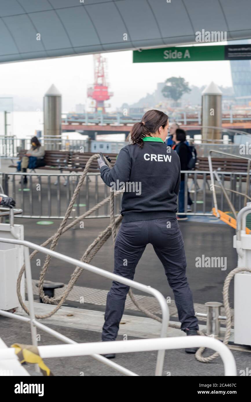 Ein weibliches Besatzungsmitglied auf einer Fähre von Sydney (Rivercat) schlingt ein Anlegeseil zu einem Poller am Barangaroo Wharf im Hafen von Sydney, Australien Stockfoto