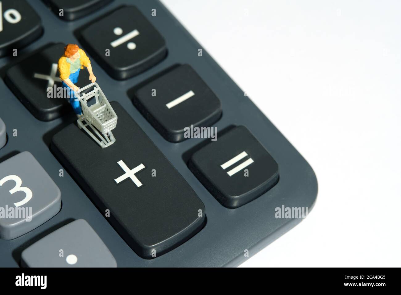 Frau mit Wagen steht auf Rechner, Berechnung der Gesamteinkauf für den Einkauf. Miniatur Menschen Figuren Spielzeug konzeptionelle Fotografie. Stockfoto