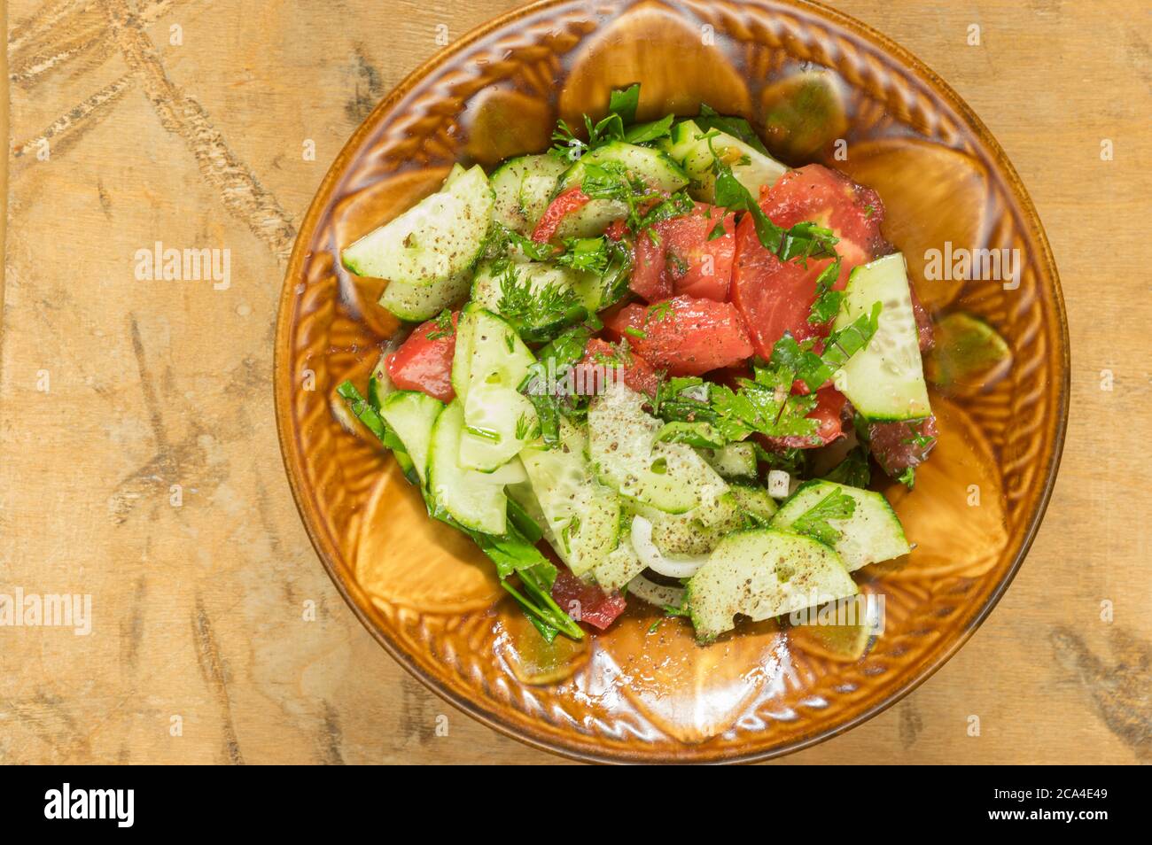Draufsicht auf Keramikschale voller veganem Salat mit roten Tomotos, Gurken, mangold, Petersilie, die auf einer schmutzigen Holzoberfläche stehen Stockfoto