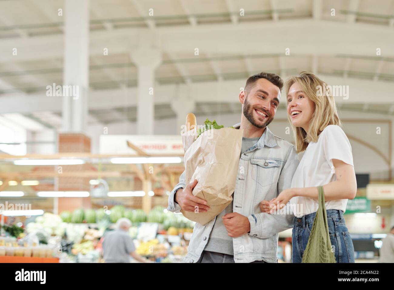 Fröhliches junges Paar, das auf dem Bauernmarkt steht und beim Einkaufen plaudert Stockfoto