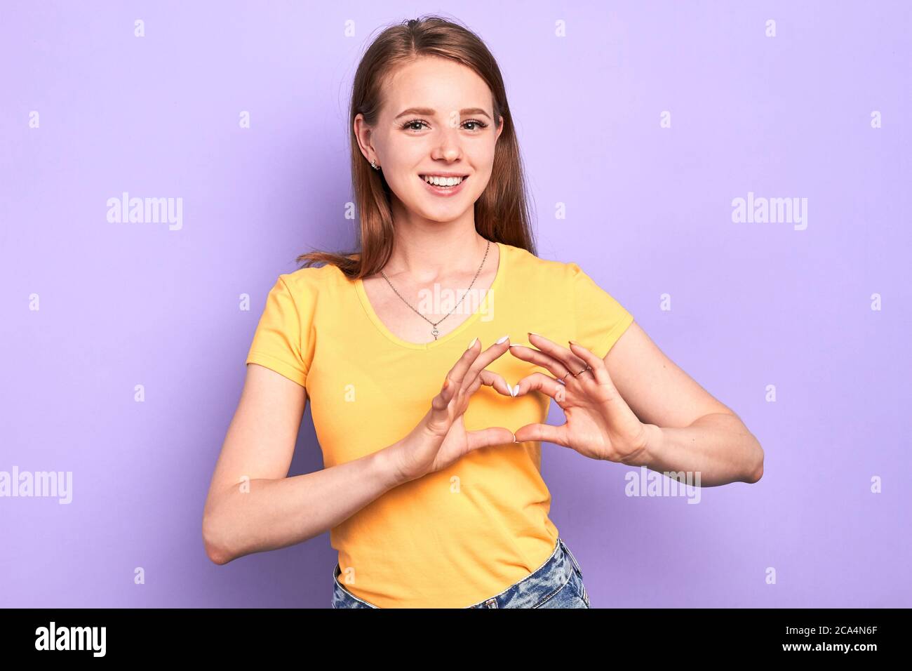 Liebenswert glücklich weiblichen Teenager macht Herz Geste mit den Händen über ihre Brust, gesteht in der Liebe zu schönen Klassenkameradin, drückt positive Gefühle und Stockfoto