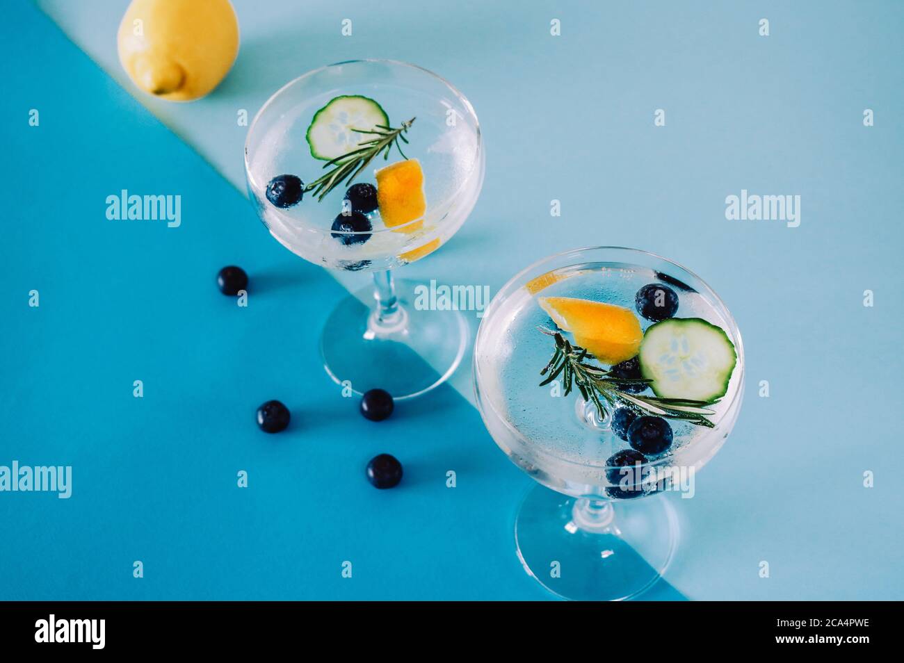 Zwei Gläser Gin-Tonic-Cocktail-Drink mit Heidelbeeren, Gurke und Rosmarin isoliert auf abstraktem, geometrischem blauem Hintergrund Stockfoto