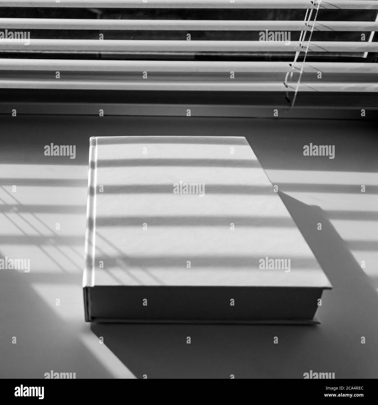 Ein weißes Buch mit scharfen Schatten liegt auf einer weißen Fensterbank Stockfoto