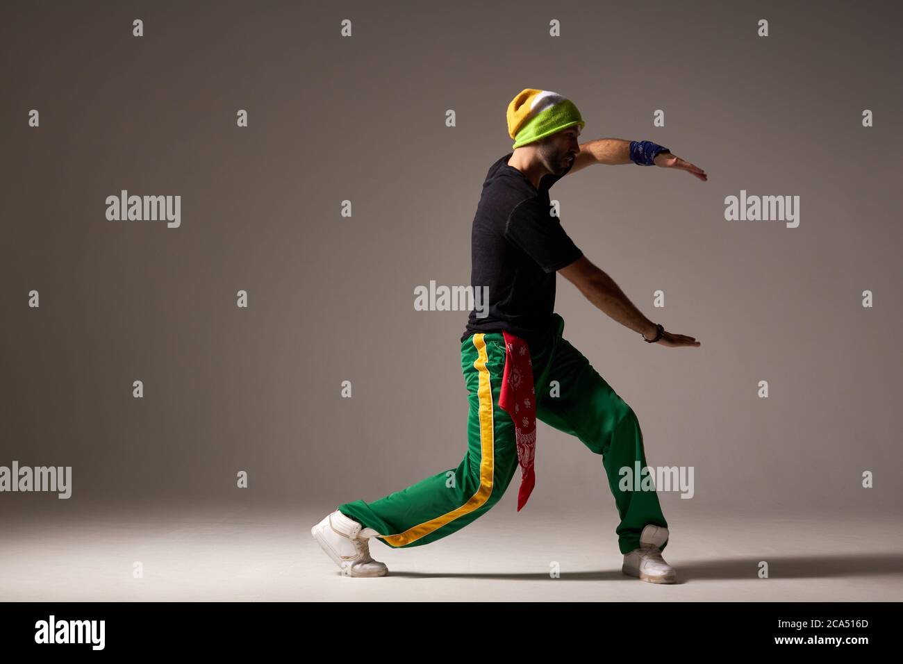Entzückte helle männliche Tänzerin in sportlichen Kleidern gekleidet, zeigt Street Dance Element im Studio, isoliert auf grauem Hintergrund, Hip Hop, rnb, moderne da Stockfoto