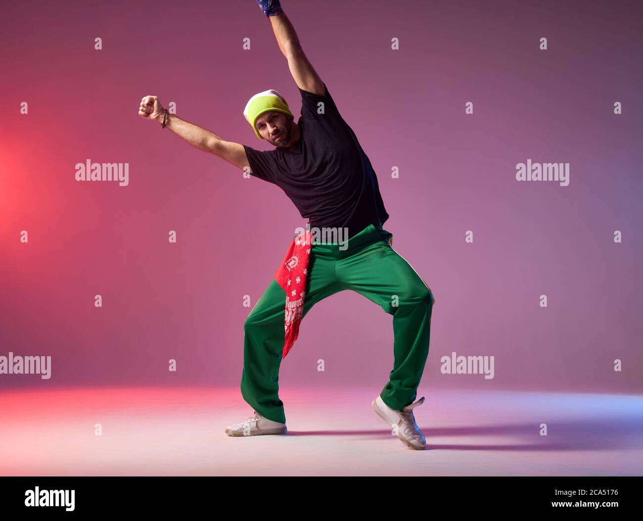 Professionelle männliche Hip Hopper in Bewegung, Stretching Hände sehr hoch, stehen auf hellem Boden der geräumigen Tanzhalle, genießen Hip Hop Tanz Stockfoto