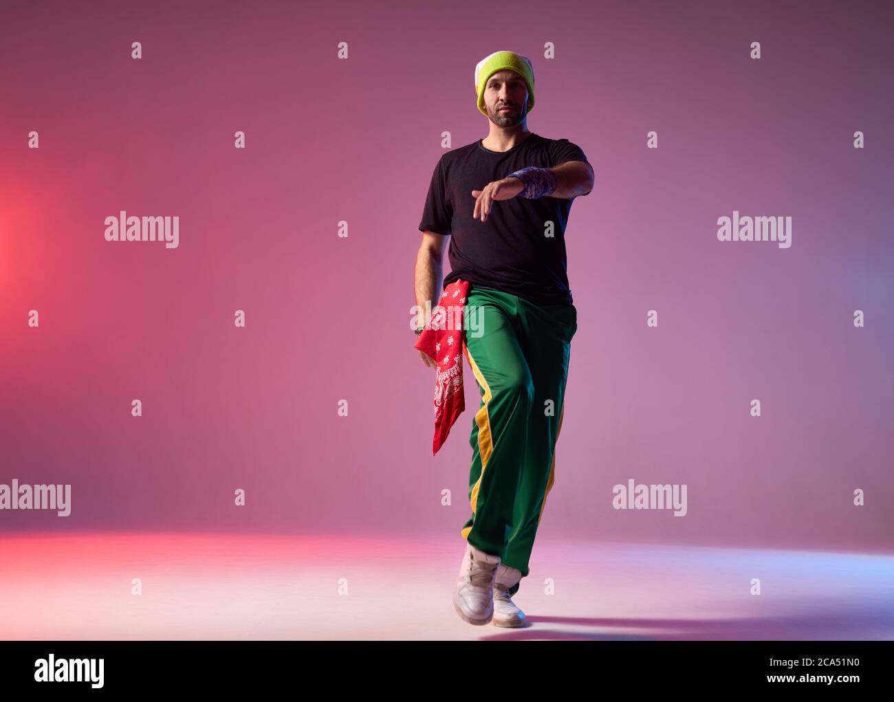 Porträt des tanzenden Mann in Sportkleidung und gelbe Kappe gekleidet, mit roten Bandana demonstriert Tanzkünste, Durchführung auf Studio-Bühne, Licht Colou Stockfoto