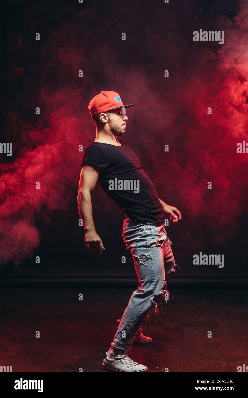 Junge gut aussehende stilvolle Mann 20-25 Jahre alt tanzen Street Dance isoliert über rauchigen Hintergrund, trägt schwarzes T-Shirt und blau zerrissene Jeans Stockfoto