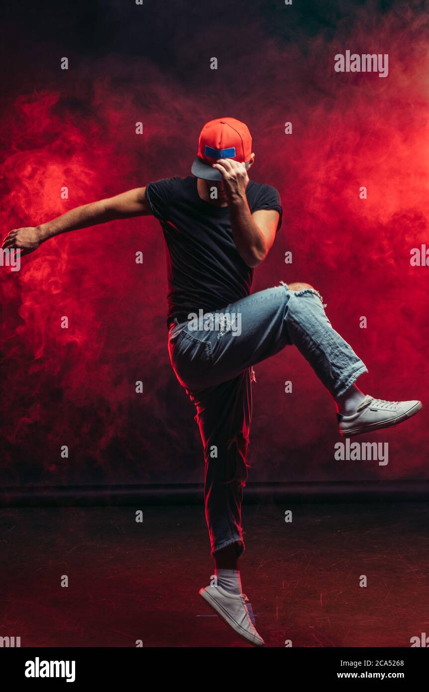 Junge gut aussehende stilvolle Mann 20-25 Jahre alt tanzen Street Dance isoliert über rauchigen Hintergrund, trägt schwarzes T-Shirt und blau zerrissene Jeans Stockfoto