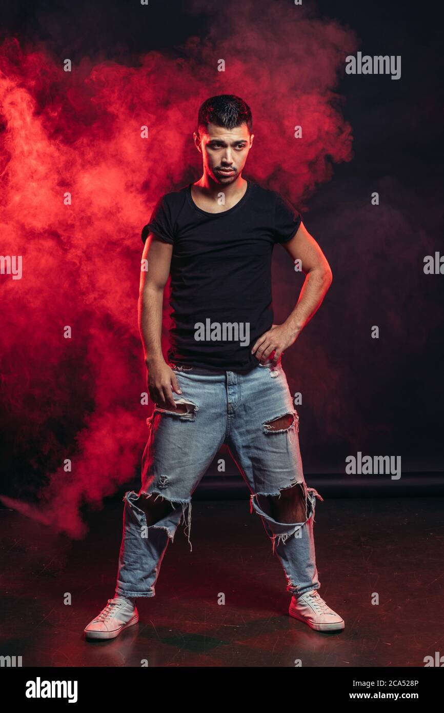 Junge gut aussehende stilvolle Mann 20-25 Jahre alt tanzen Street Dance isoliert über rauchigen Hintergrund, trägt schwarzes T-Shirt und blau zerrissene Jeans Stockfoto