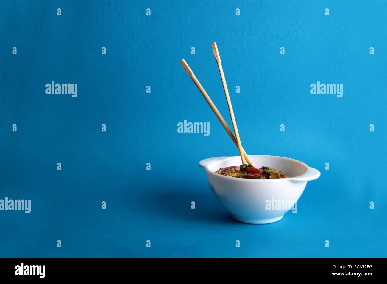 Eine Schüssel mit Wok-Nudeln und Essstäbchen isoliert auf blauem Hintergrund. Das Bild enthält den Kopierbereich Stockfoto