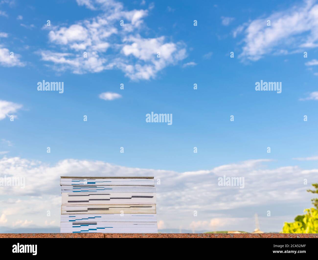 Bücher auf einer roten Steinmauer gegen einen schönen blauen Himmel mit weißen Wolken gestapelt Stockfoto