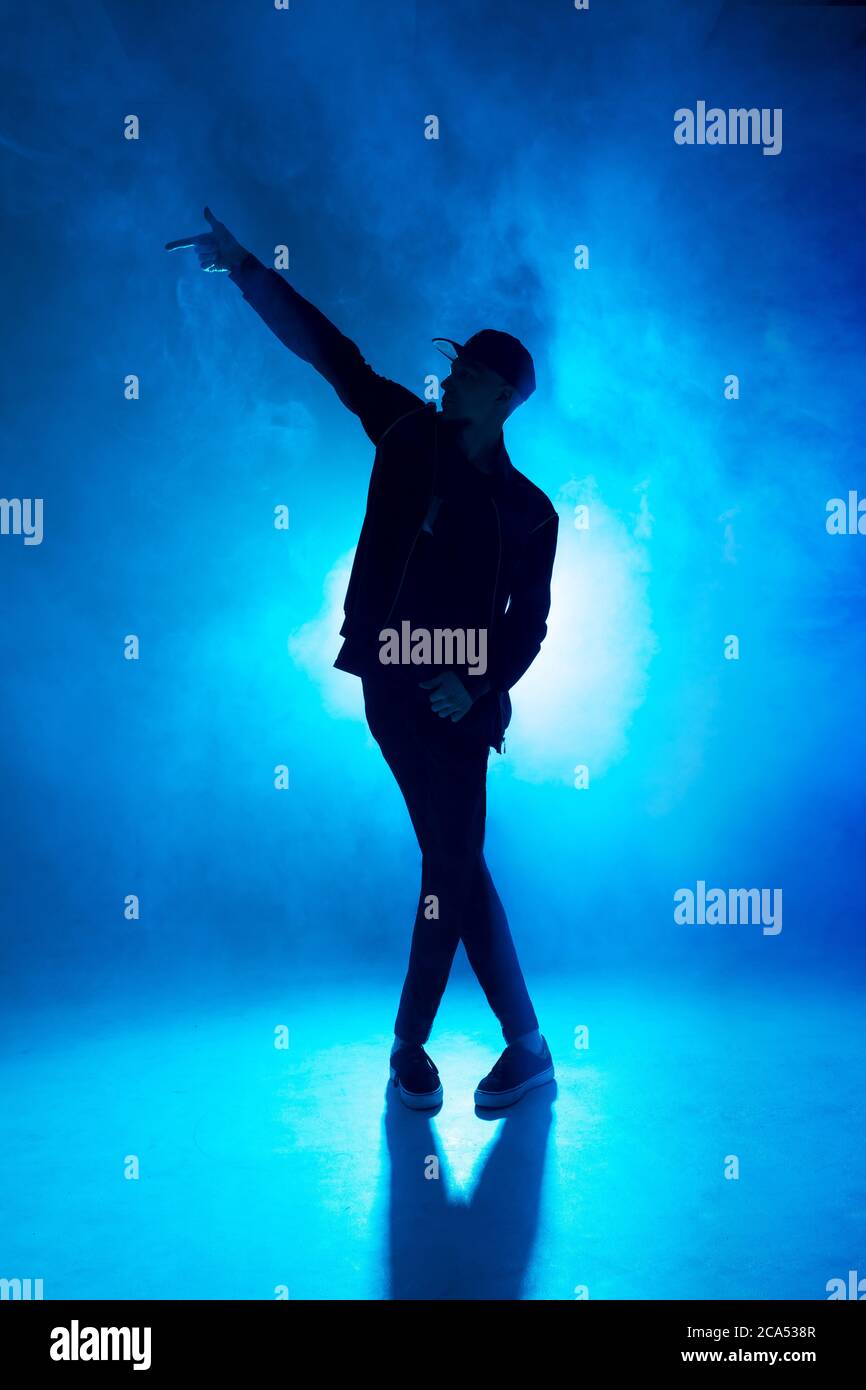 Freizeit, Lifestyle, Hobby und Sport. Professionelle männliche Tänzerin tanzt im Nachtclub mit Rauch und blauen Neonlichtern mit Lichtern in der Mitte Stockfoto