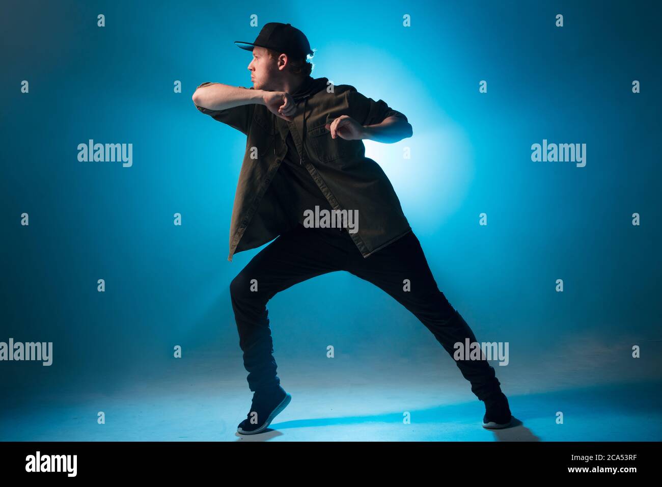 Sportlich moderner Hip-Hop-Tänzer in urbaner Kleidung zeigt seinen Tanz auf blauem Studiohintergrund. Stockfoto