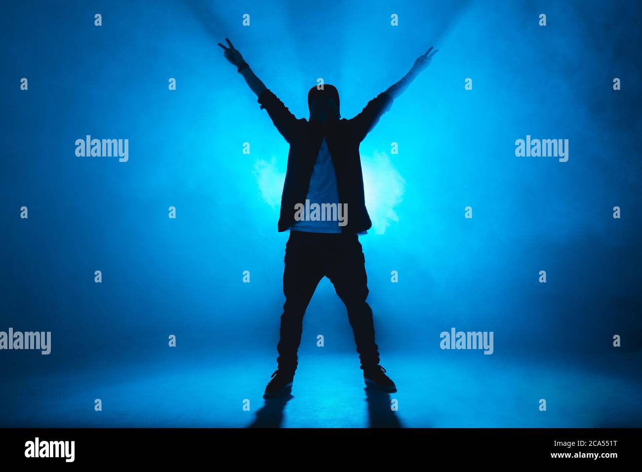 Sportlich moderner Hip-Hop-Tänzer in urbaner Kleidung zeigt seinen Tanz auf blauem Studiohintergrund. Stockfoto