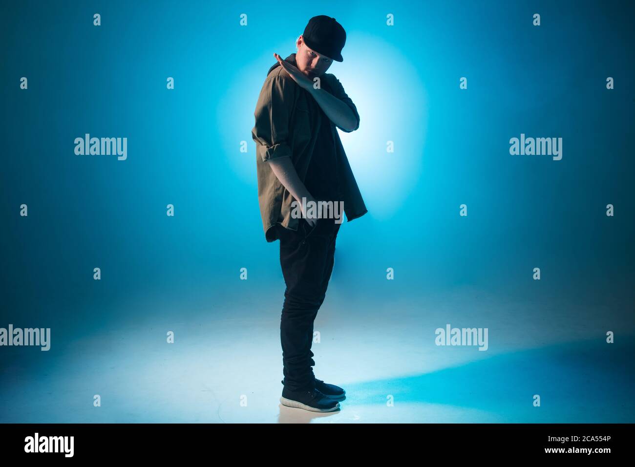 Sportlich moderner Hip-Hop-Tänzer in urbaner Kleidung zeigt seinen Tanz auf blauem Studiohintergrund. Stockfoto