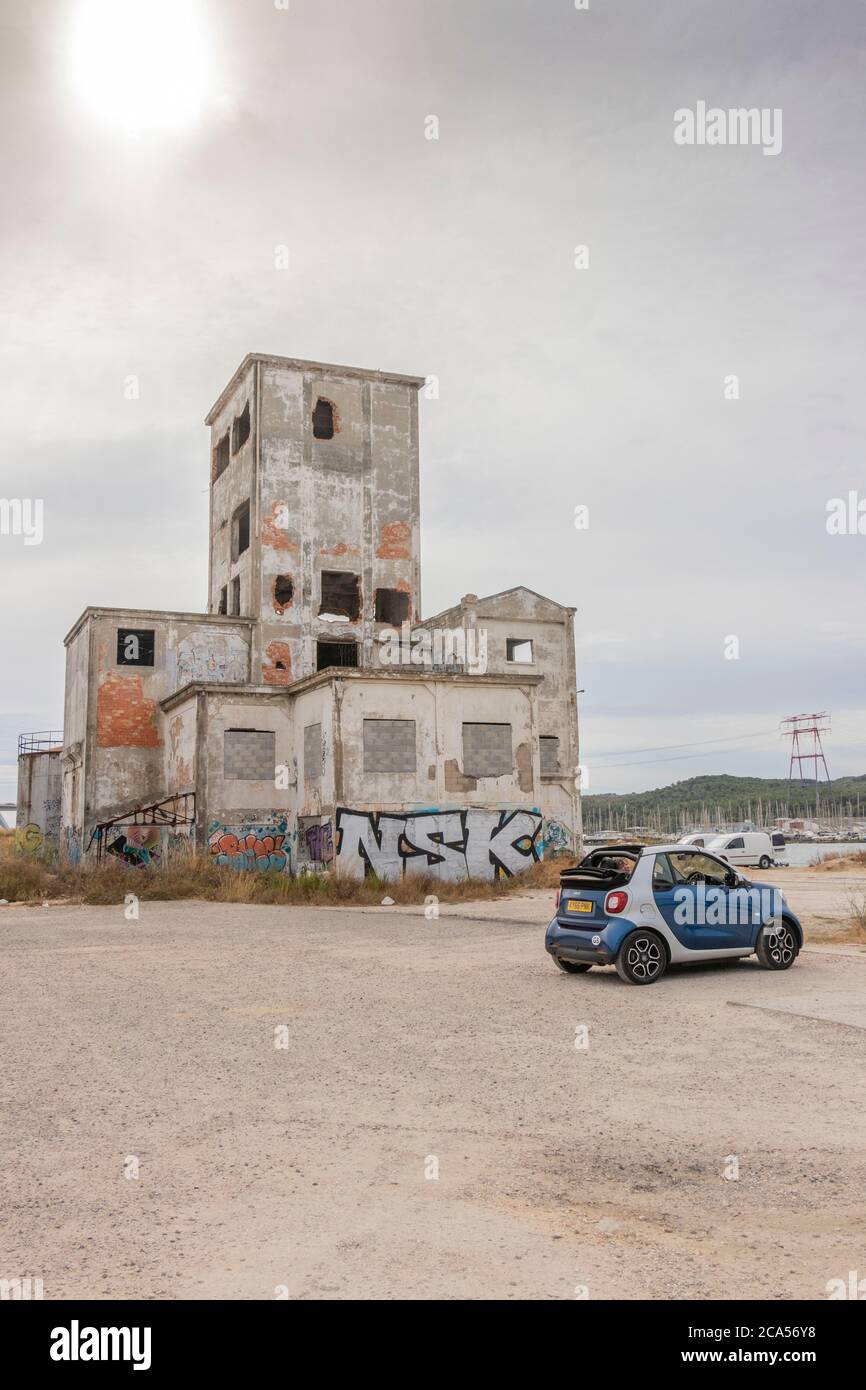 Soft top Blue Smart Car fortwo mit verderbenem Hafengebäude am Flussufer in der Nähe von Viaduc de Caronte, 13117 Martigues, Südfrankreich Stockfoto