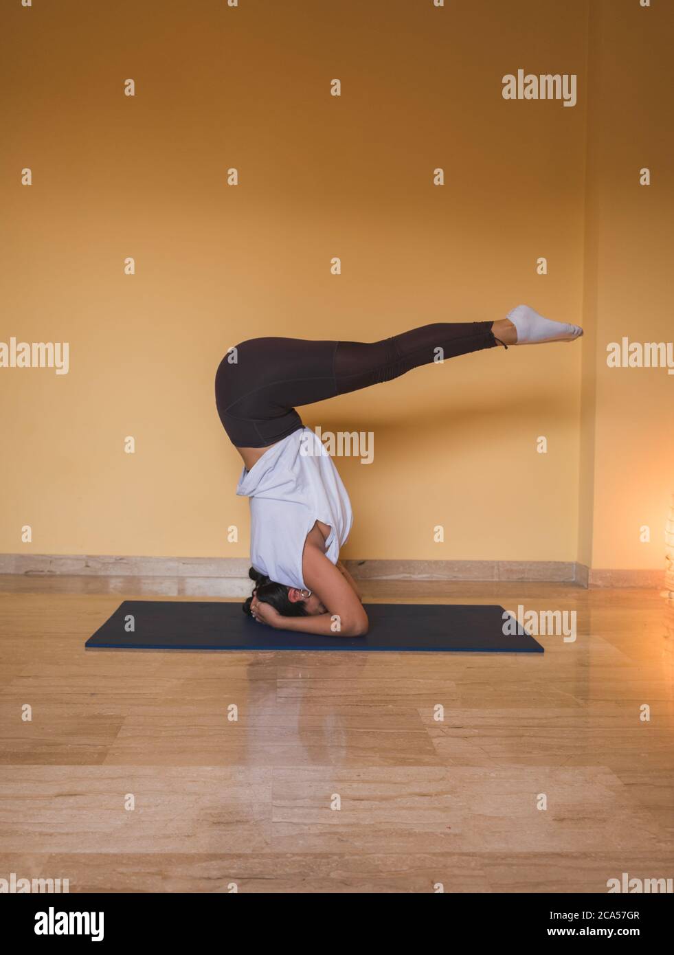 Anonyme Frau beginnt unterstützte Kopfstand Pose. Seitenansicht der schlanken Frau, die Yoga im gemütlichen Wohnzimmer tagsüber zu Hause macht. Stockfoto