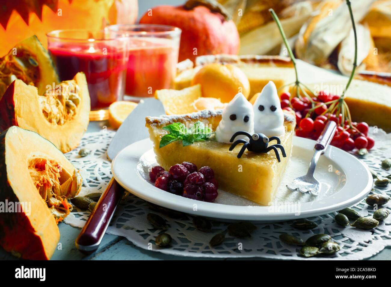 Hausgemachte halloween Kürbiskuchen mit schwarzer Spinne und kleinen Geistern auf weißem Teller Nahaufnahme. Kerzen und Jack-o-Laterne auf dem Hintergrund. Traditionelles Urlaubsessen Stockfoto