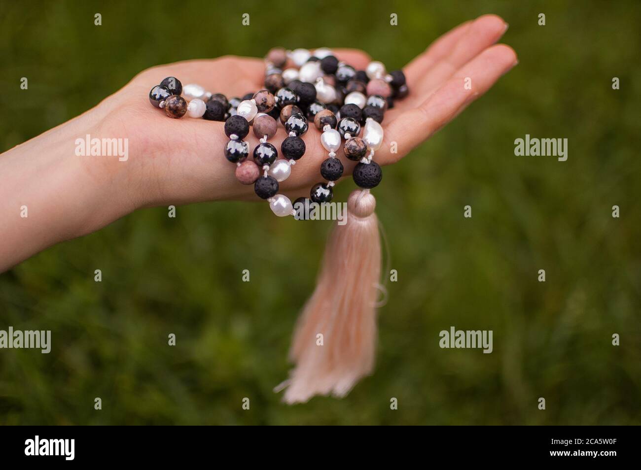 Weibliche Hand hält ein buddhistisches Japa mala aus 108 Natursteinen Perlen für Meditation auf grünem Gras Hintergrund Stockfoto