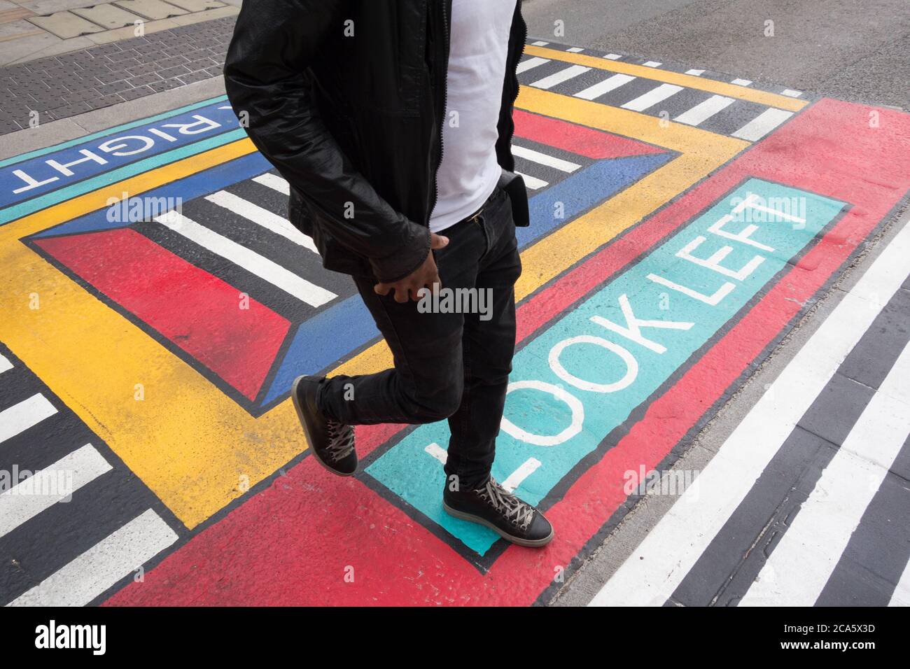 Nahaufnahme eines Mannes, der die geometrischen Fußgängerübergänge des französischen Künstlers Camille Walala vor der U-Bahnstation White City im Westen Londons durchquert Stockfoto