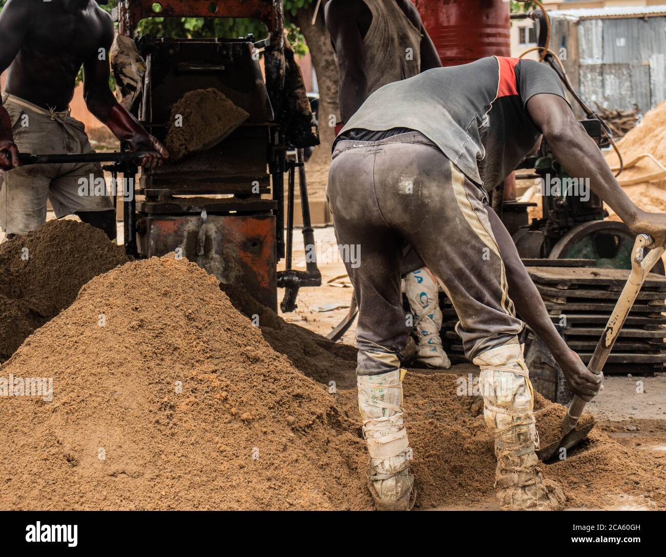 Afrikanische Arbeiter in schmutzigen Kleidern schaufeln Sand und arbeiten mit Baustoffen. Stockfoto