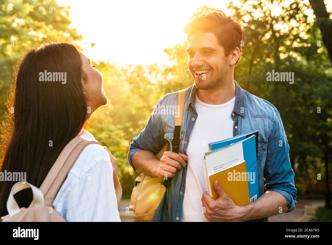 Bild von fröhlichen multikulturellen Studenten reden und lächeln einander beim Spaziergang im grünen Park Stockfoto