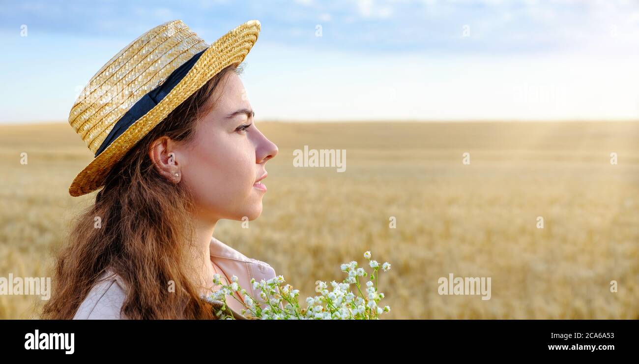 Profilportrait einer jungen Frau im Strohhut und mit Blumenstrauß Stockfoto